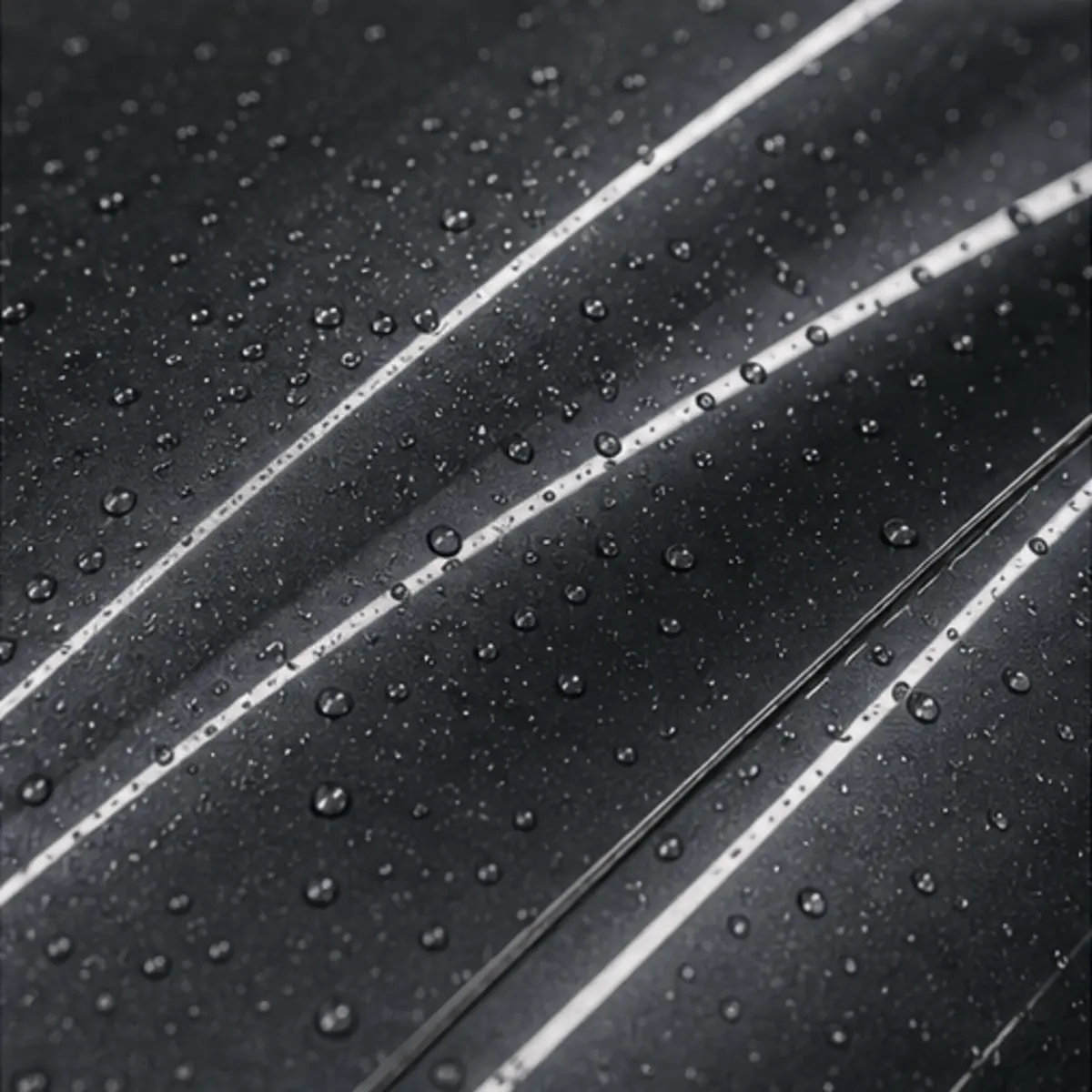 Extreme close-up of the sedan's dark grey paint surface with water droplets and reflected linear studio lights, showing finish quality after correction work.